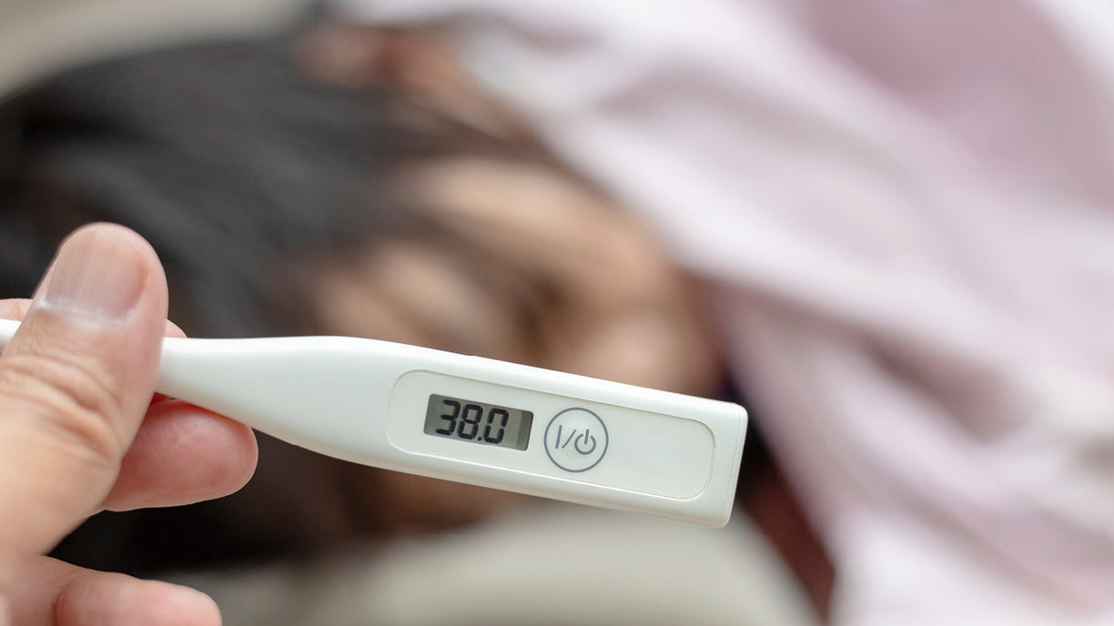 Une mère prend la température de son bébé avec un thermomètre. L’appareil indique 38 degrés, tandis que la mère observe attentivement son enfant.
