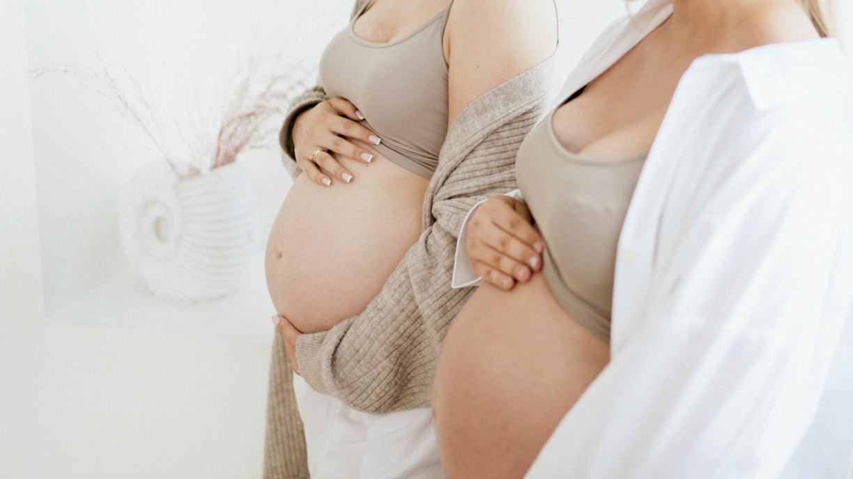 Deux femmes enceintes posant les mains sur leur ventre, montrant l’importance de rester attentive aux signes et symptômes pendant la grossesse.