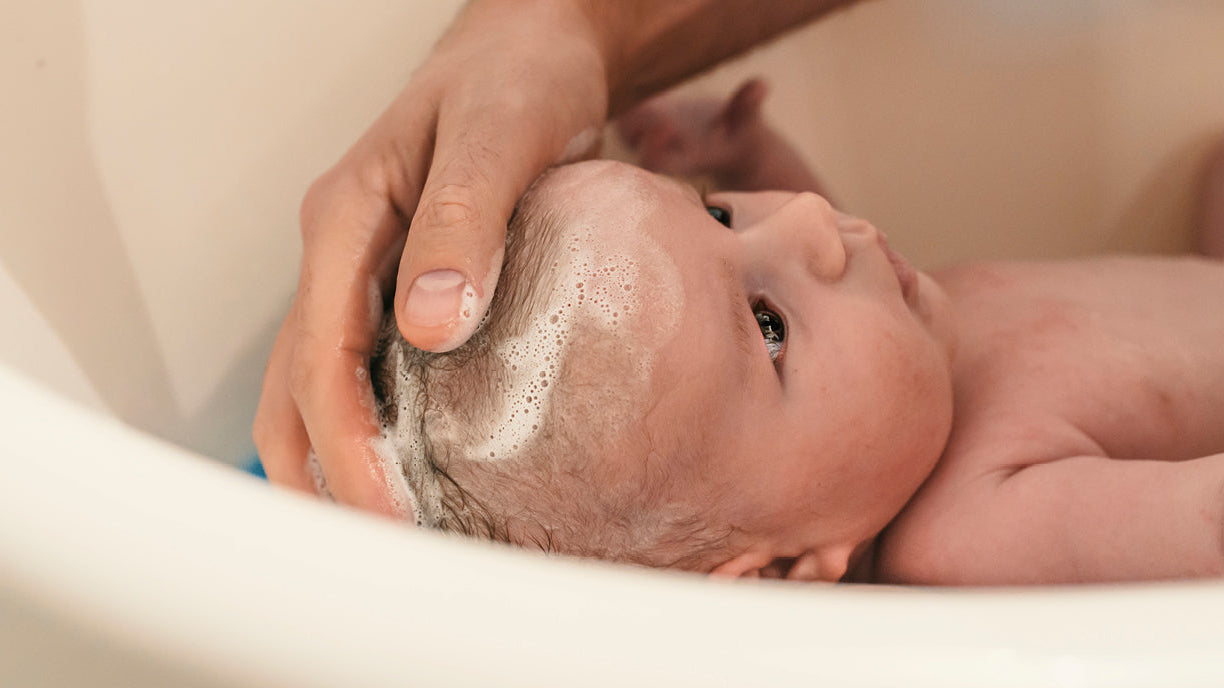 Bébé prenant son bain, soutenu avec douceur par un parent — un moment de soin et de tendresse illustrant l’importance de la préparation et du calme lors du bain du nouveau-né.