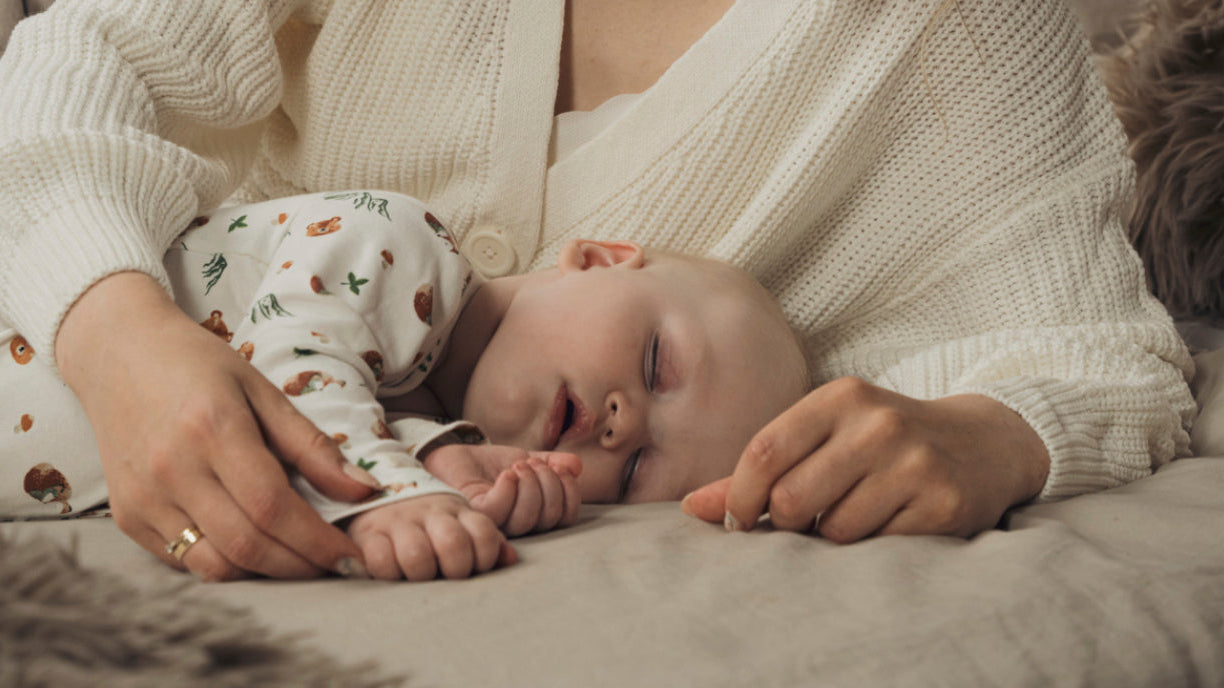 Bébé endormi allongé dans les bras de sa mère, symbole de douceur et de soutien pour une croissance saine et une colonne vertébrale bien développée.