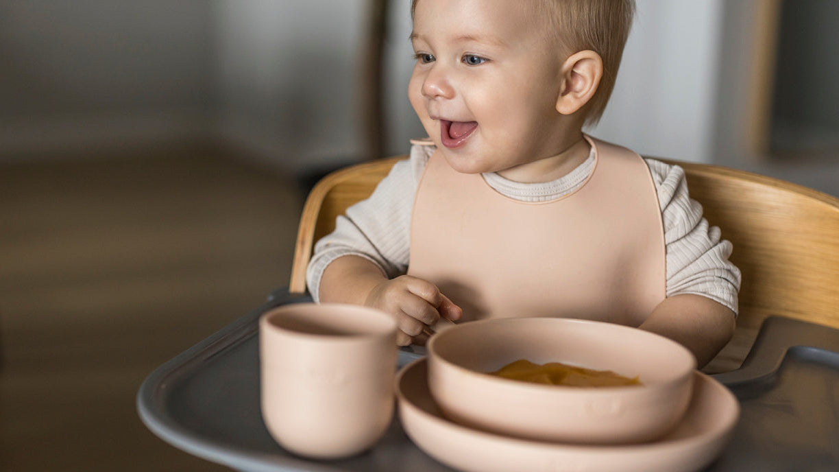 Bébé assis dans sa chaise haute, utilisant le set de repas Difrax Lovi, dégustant un repas préparé avec du lait infantile