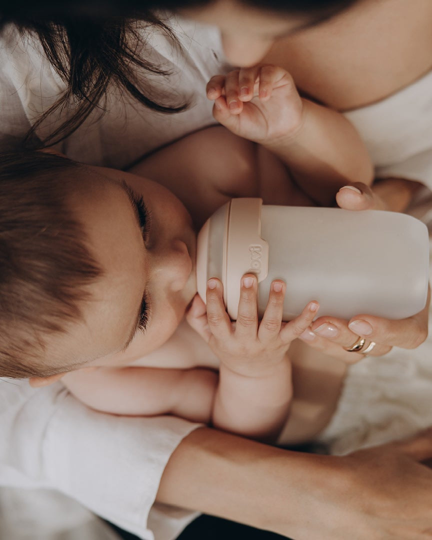 Baby lies in arms of mothers. Baby is drinking milk form a baby bottle.