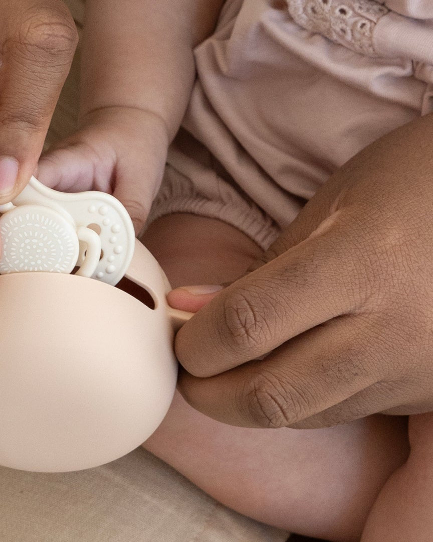 Une jeune fille est assise à une table de déjeuner. Elle porte leBoite à sucette en silicone Difrax LOVI nu