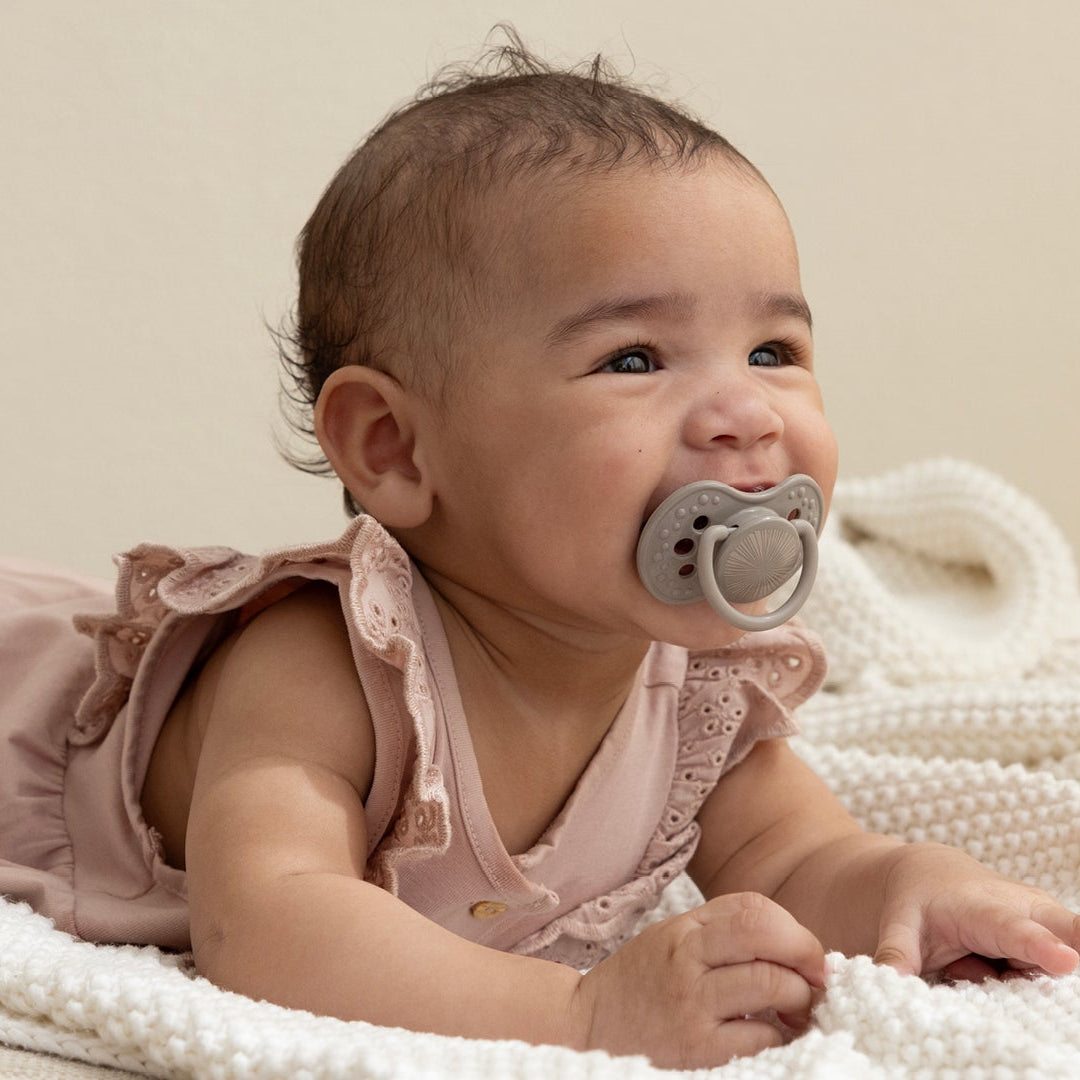 Un bébé de 6 mois est allongé sur le ventre avec un grand sourire. Elle a une sucette Difrax LOVI de la collection Harmony