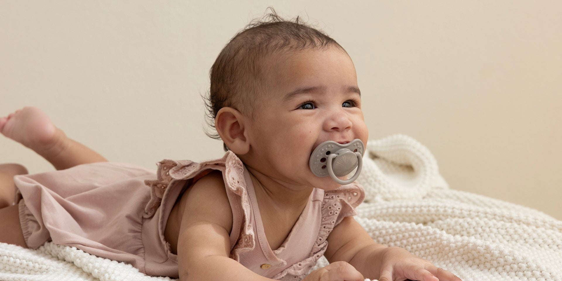 Un bébé de 6 mois est allongé sur le ventre avec un grand sourire. Elle a une sucette Difrax LOVI de la collection Harmony