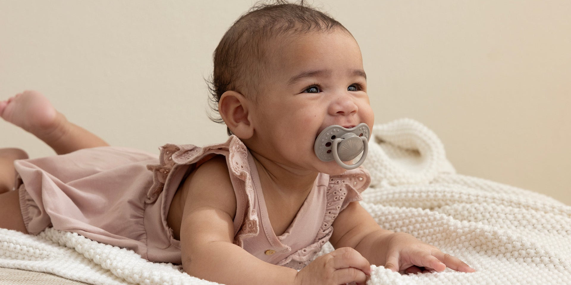Un bébé de 6 mois est allongé sur le ventre avec un grand sourire. Elle a une sucette Difrax LOVI de la collection Harmony