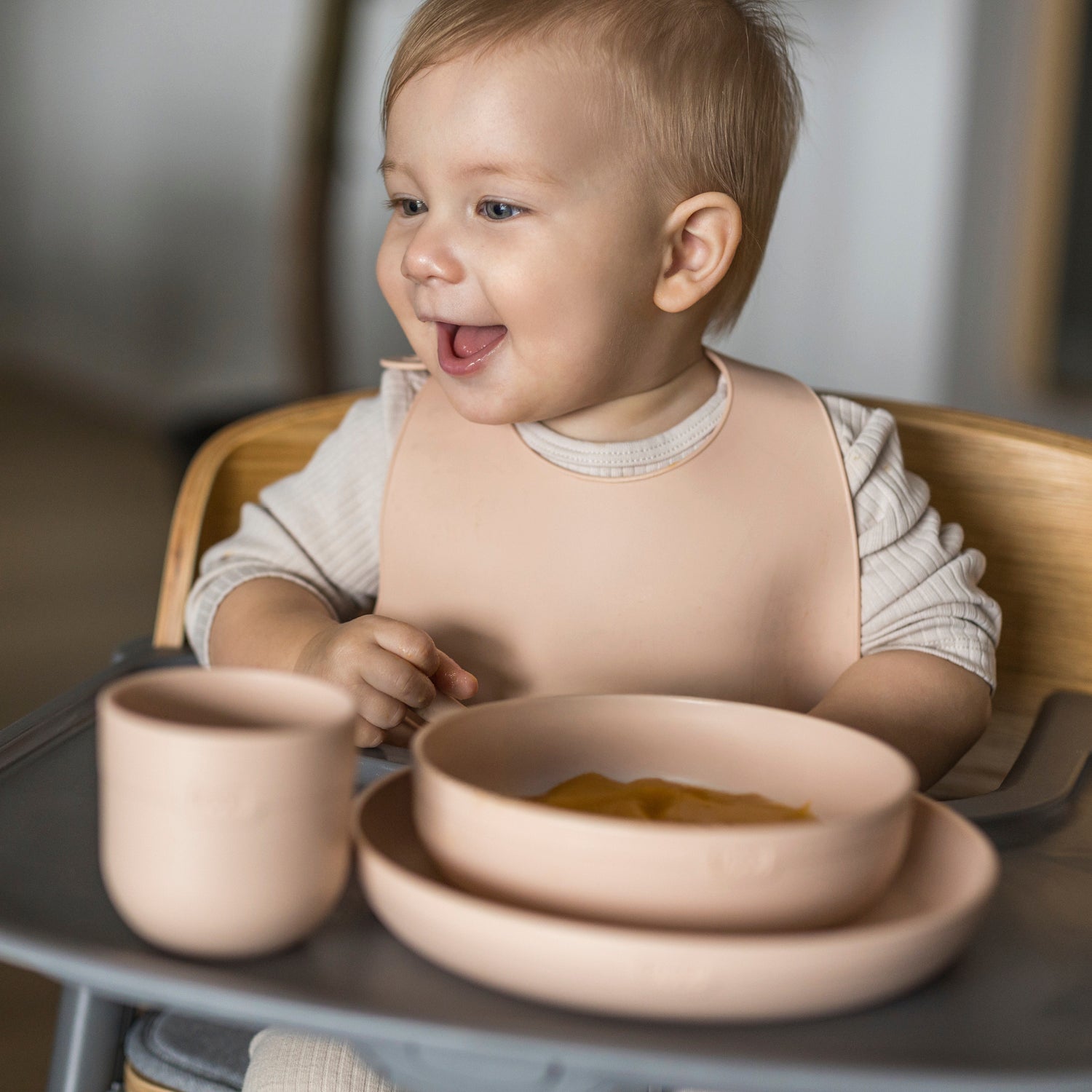Bébé dans une chaise haute avec Difrax LOVI Nude – ensemble repas et boissons et bavoir.