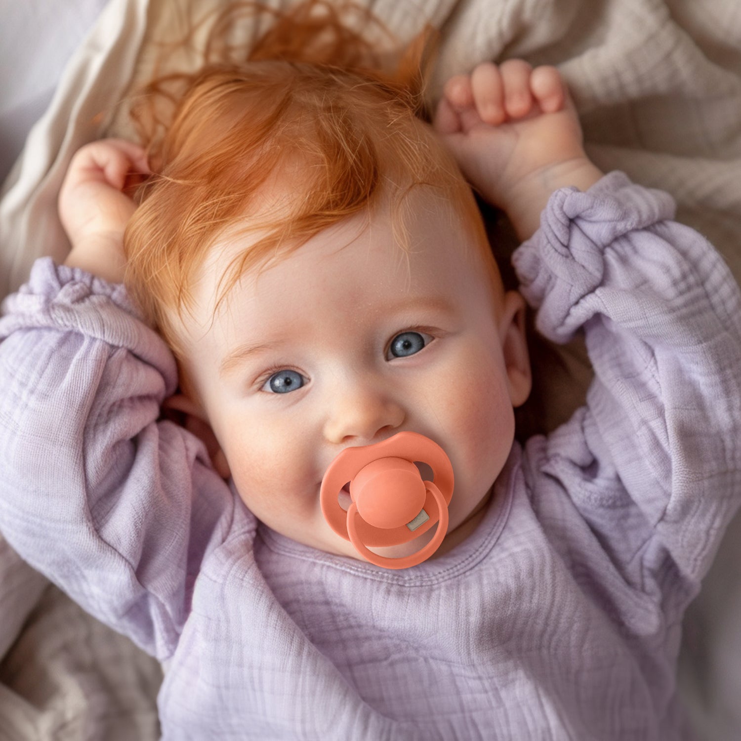 Un bébé heureux couché avec la sucette Orange dynamic dans la bouche