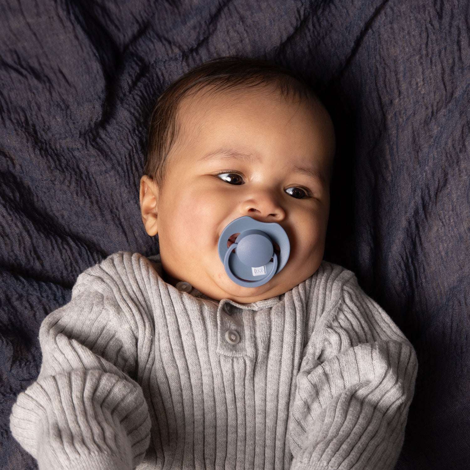 Un petit garçon heureux couché avec la Sucette dynamique Prime bleu.