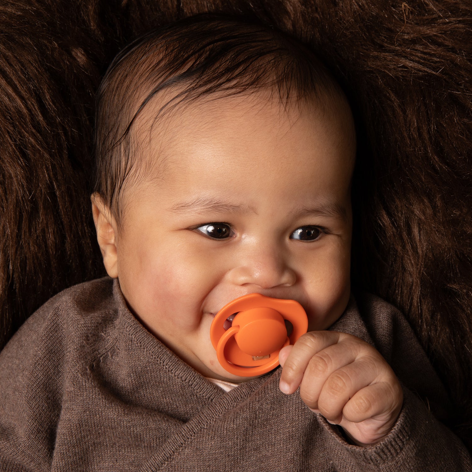 Un bébé heureux couché avec la sucette Orange dynamic dans la bouche
