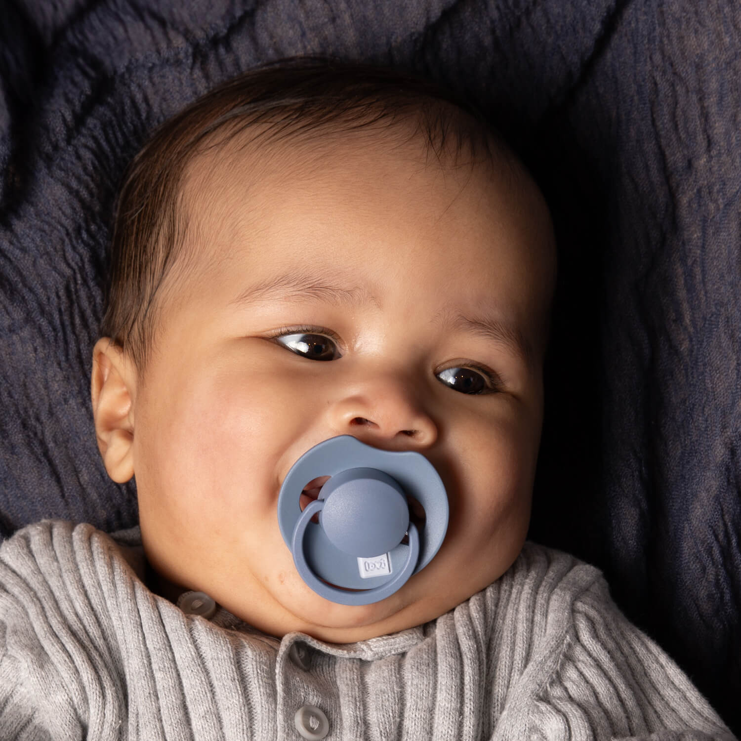 Un bébé heureux couché avec la sucette bleue dynamic dans la bouche