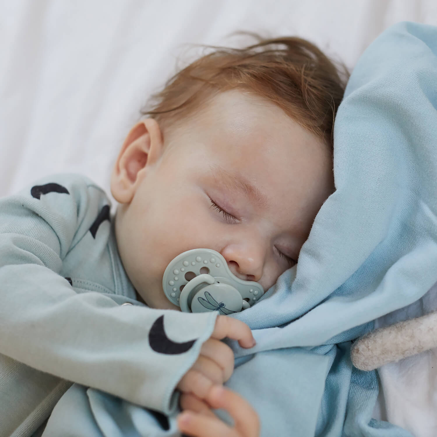 Un petit garçon qui dort avec la sucette verte.