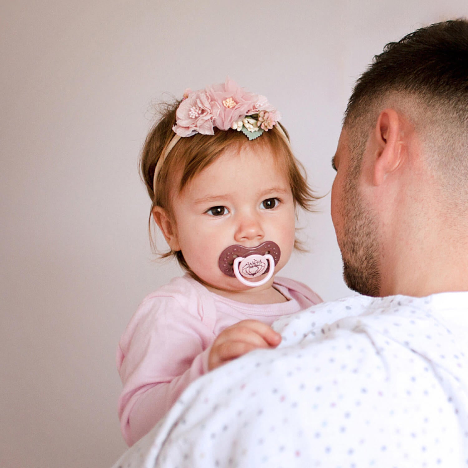 Un papa tient son enfant avec la sucette dynamique violette dans la bouche.