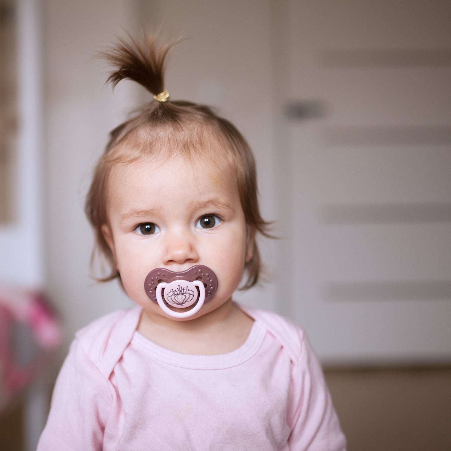 Un enfant en bas âge avec la sucette botanique violette dans sa bouche.