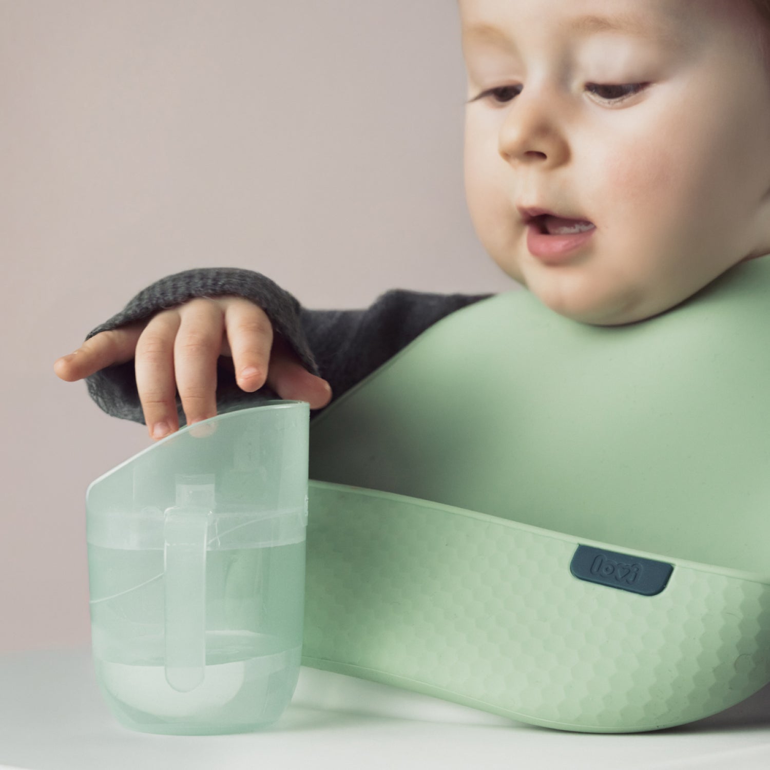 Enfant avec gobelet d’apprentissage Genius vert et bavoir assorti de LOVI