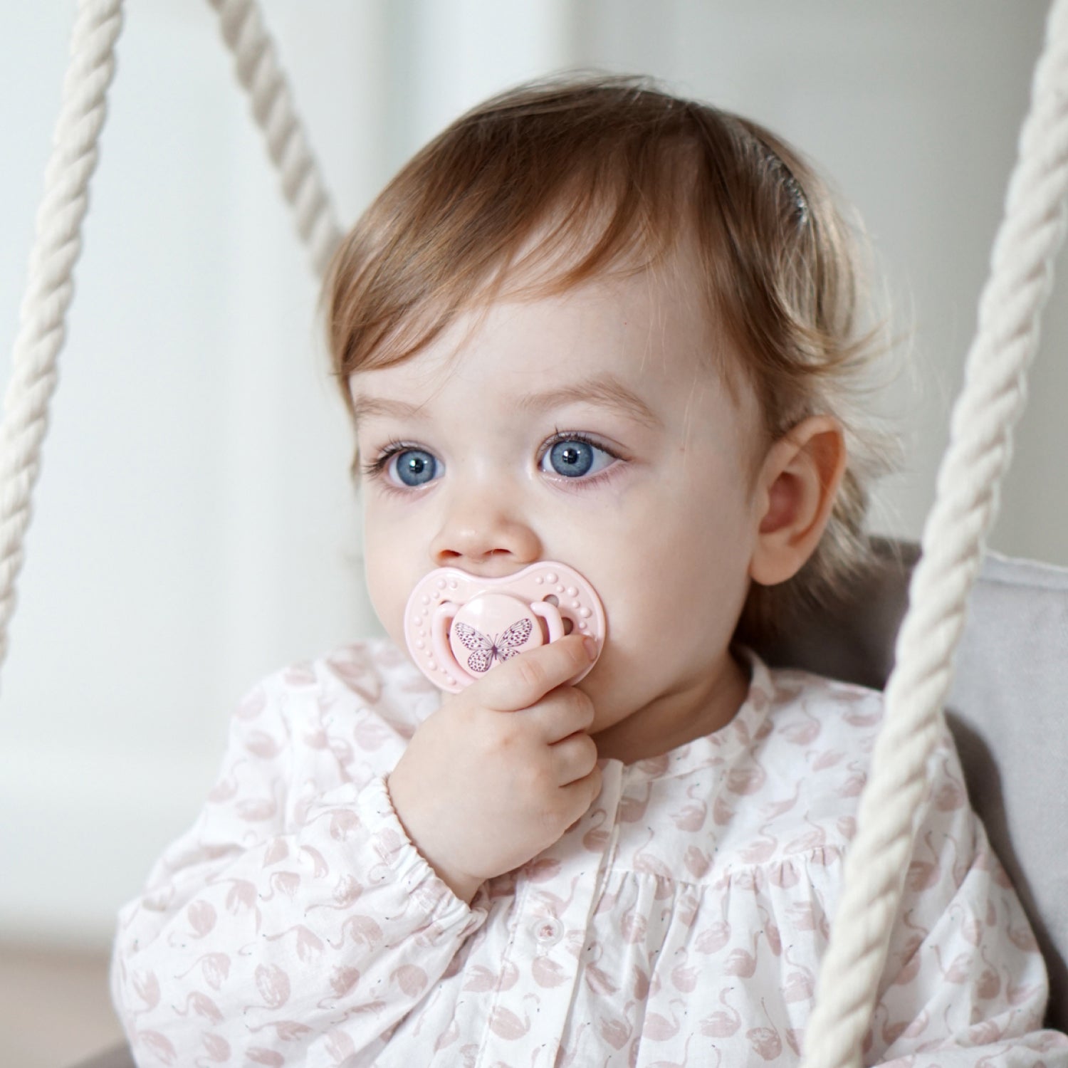 Un enfant en bas âge assis avec la sucette botanique rose dans sa bouche.
