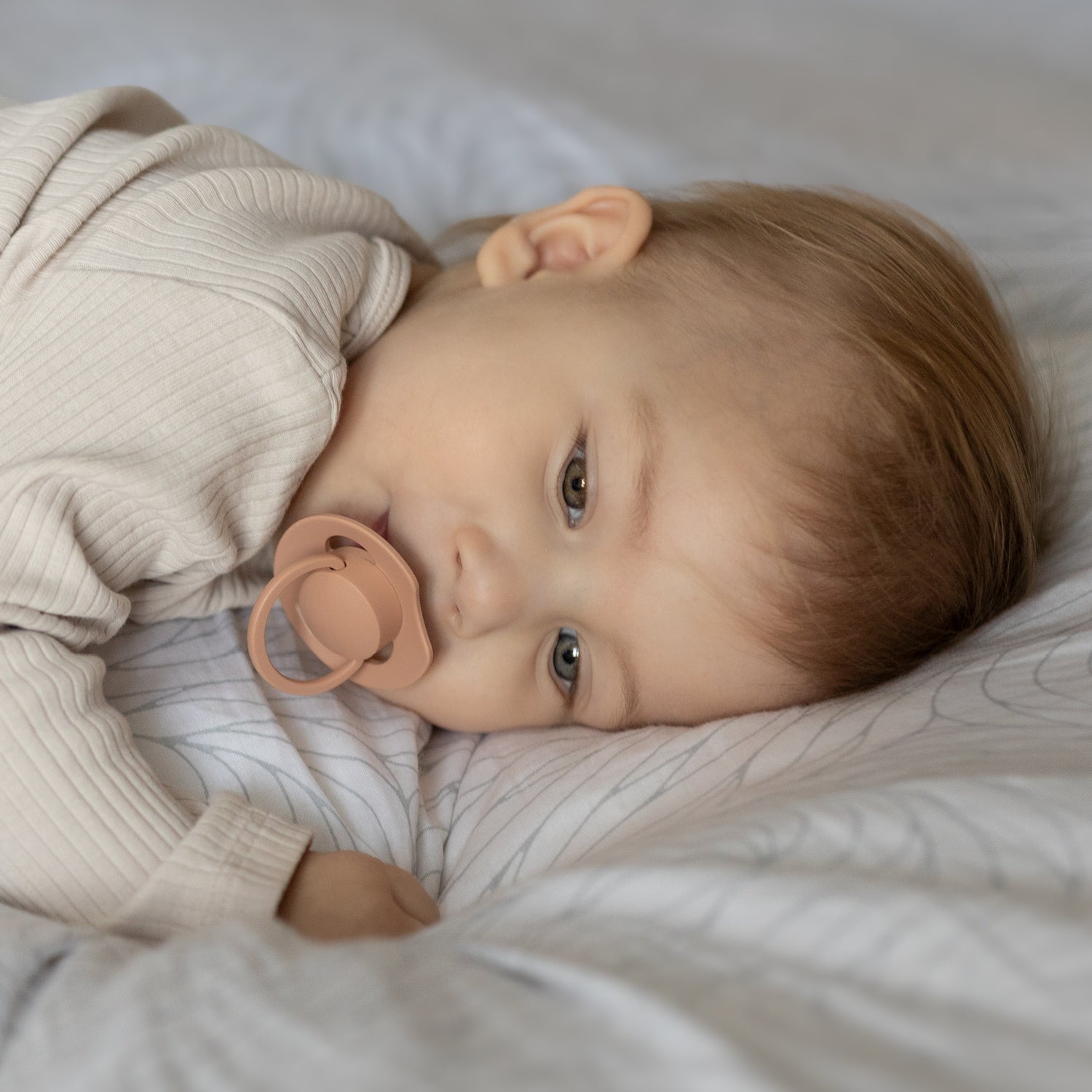 Un nourrisson allongé sur le lit avec la sucette Prime Nude Blush