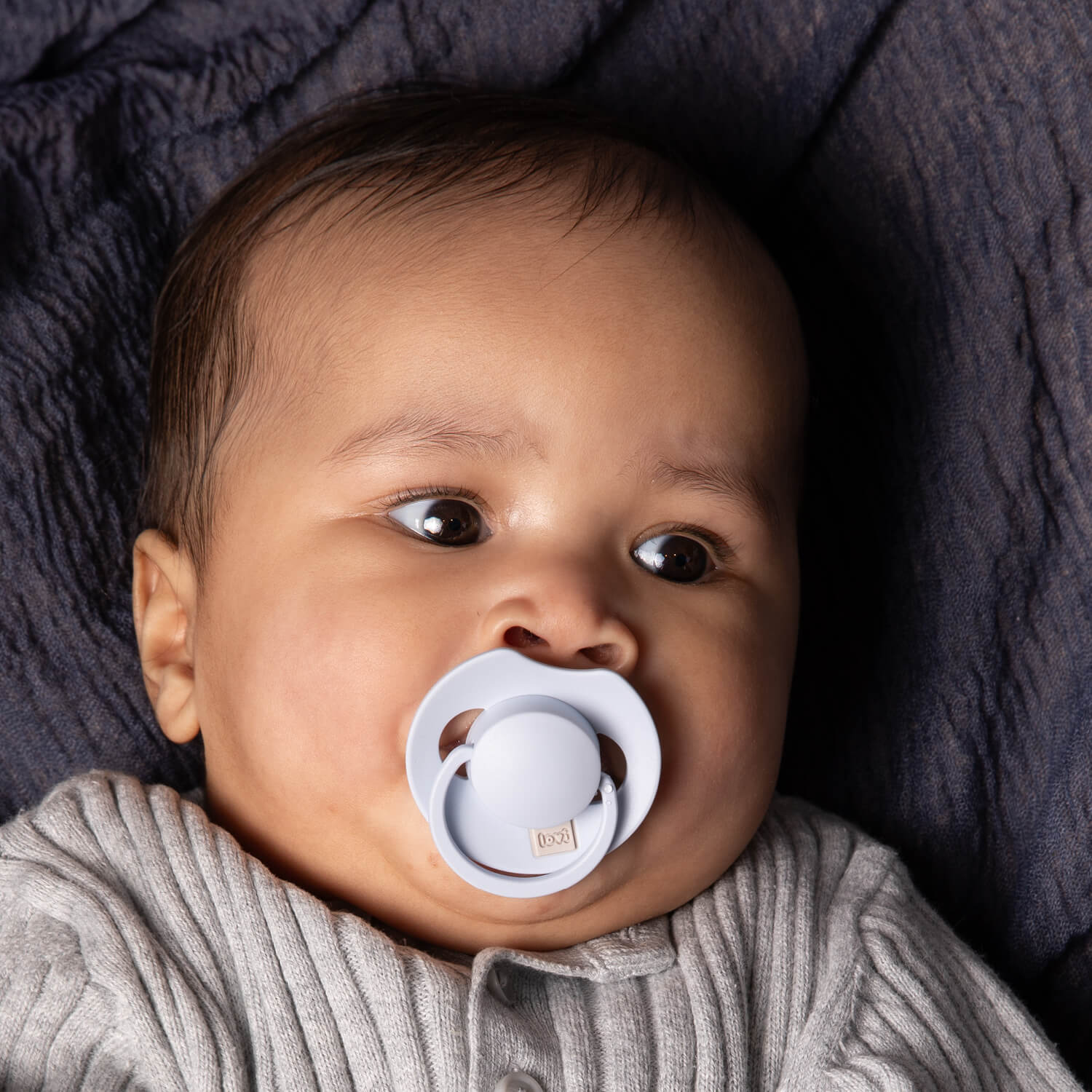 Un petit garçon heureux couché avec la Sucette dynamique Prime babybleu