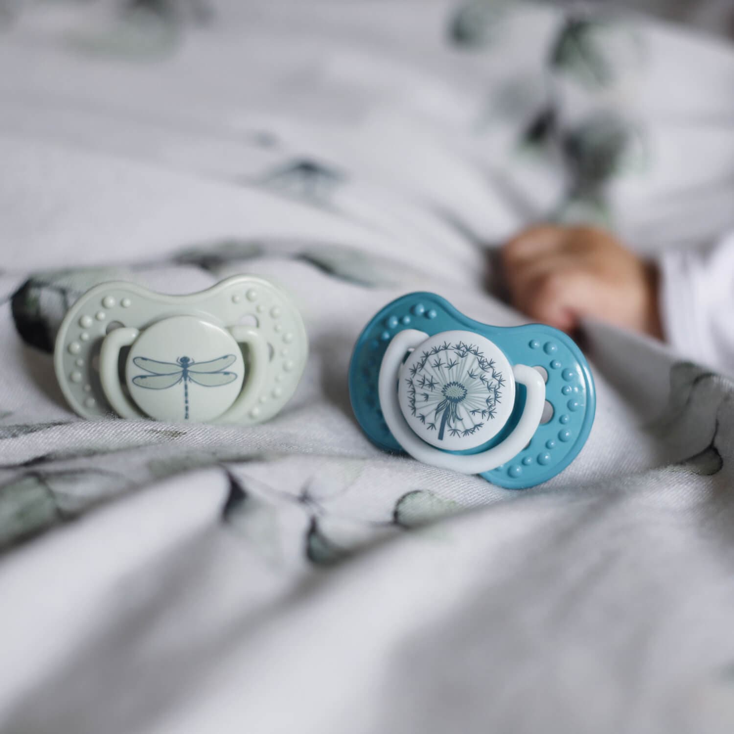 2 Sucettes botanic dynamiques dans les couleurs vert et bleu allongées sur le lit