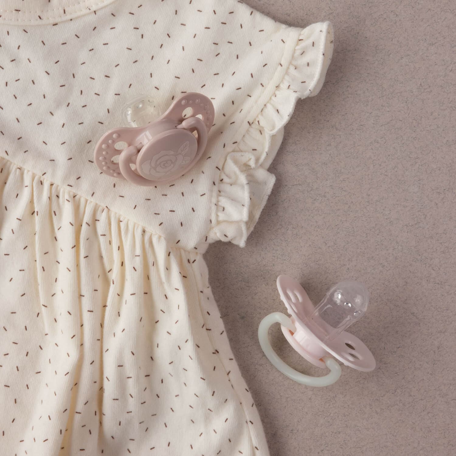 Deux sucettes roses pastel avec robe de bébé à motifs délicats et volants