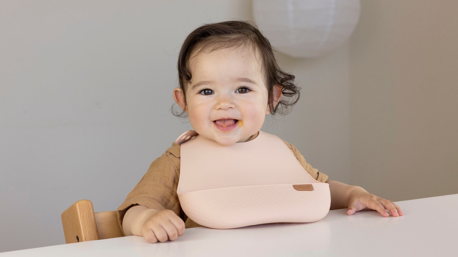  Un bambin heureux est assis à table avec un bavoir en silicone nude.