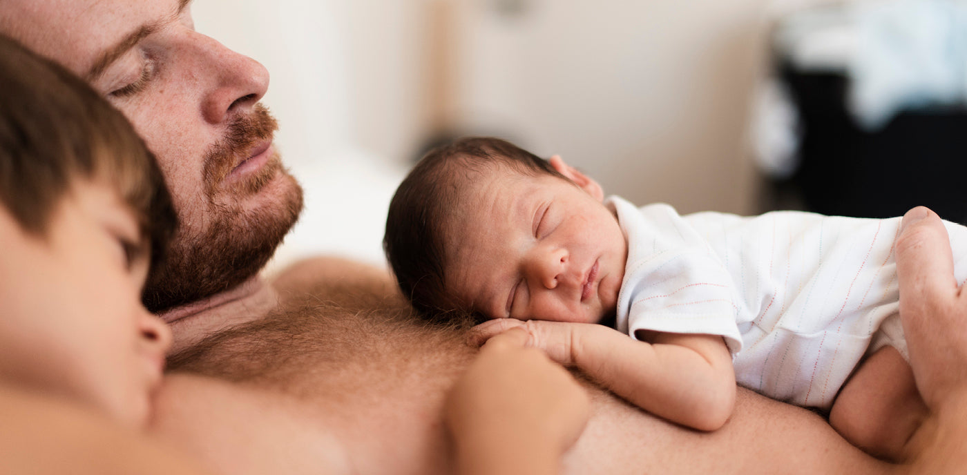 le père avec deux enfants, le bébé dort sur lui et l'autre est assis à côté de lui