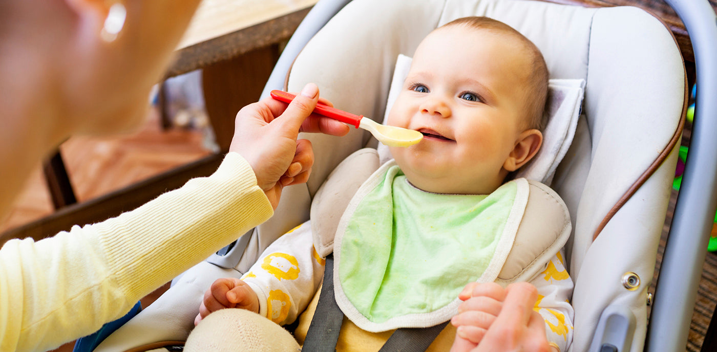 Une mère nourrit son petit enfant avec une cuillère pour bébé, en lui donnant à manger avec douceur pendant que l’enfant est assis et ouvre la bouche pour manger.