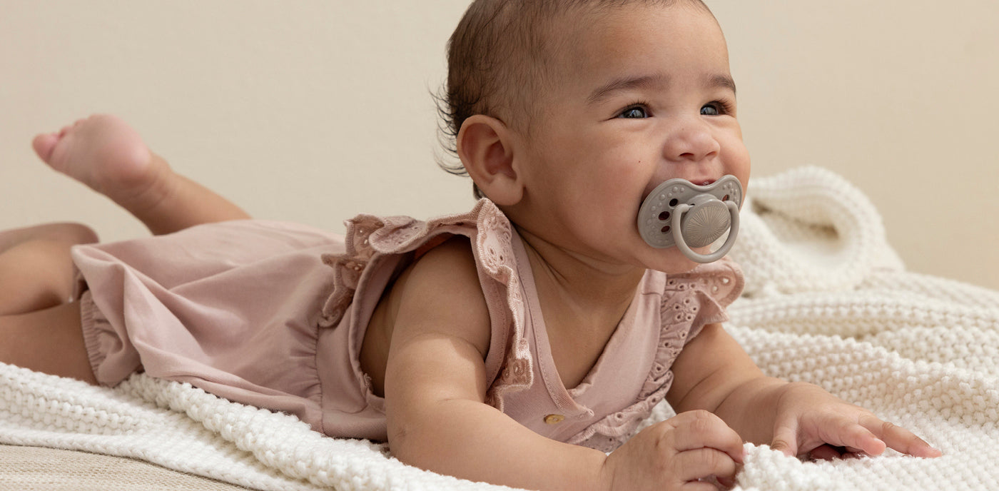 Bébé allongé sur le ventre avec une sucette en bouche, calme et détendu.