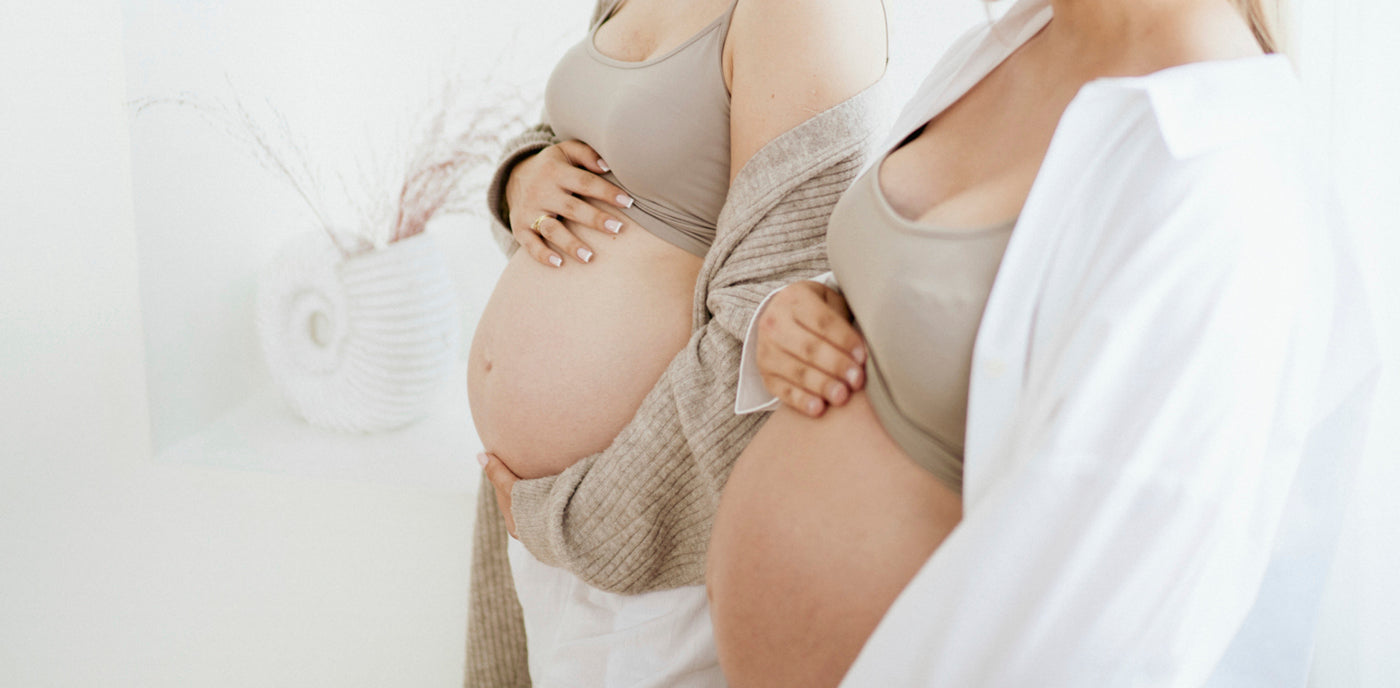 Deux femmes enceintes posant les mains sur leur ventre, montrant l’importance de rester attentive aux signes et symptômes pendant la grossesse.