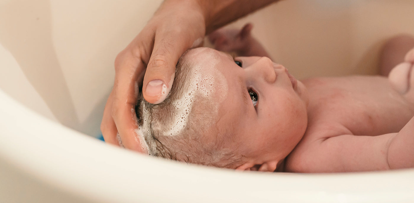 Bébé prenant son bain, soutenu avec douceur par un parent — un moment de soin et de tendresse illustrant l’importance de la préparation et du calme lors du bain du nouveau-né.
