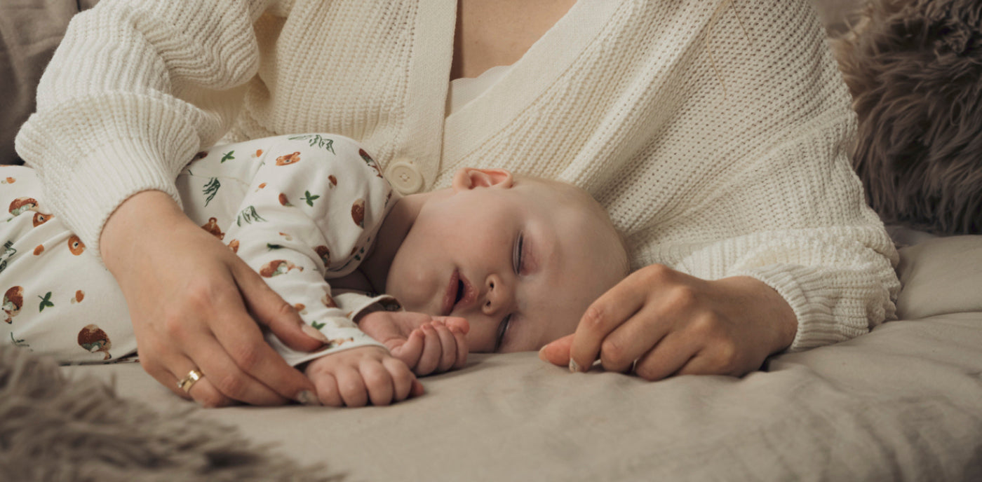 Bébé endormi allongé dans les bras de sa mère, symbole de douceur et de soutien pour une croissance saine et une colonne vertébrale bien développée.