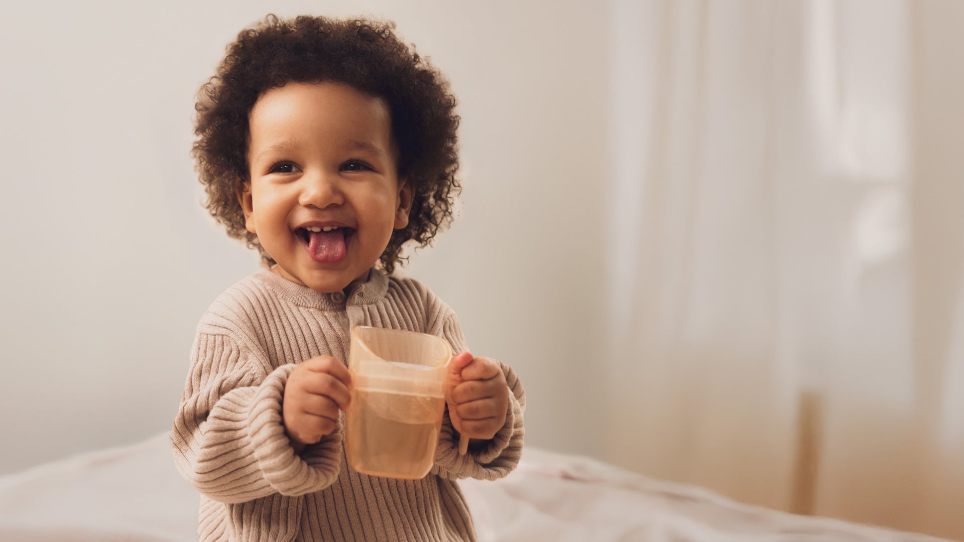 Bébé buvant dans un gobelet éducatif Genius, assis sur une chaise haute, en apprenant à s’hydrater de manière autonome.