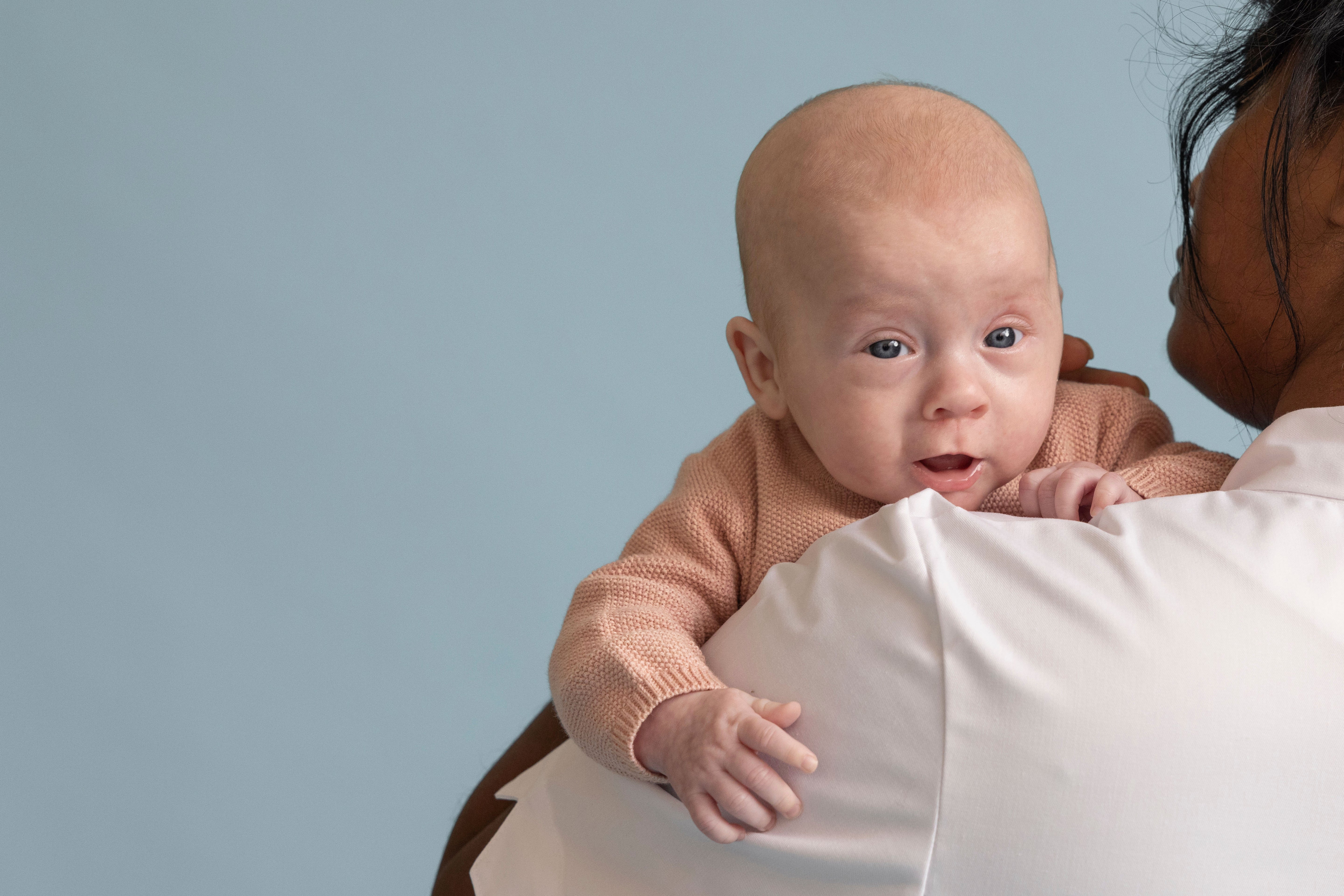 Bébé aux yeux bleus regardant par-dessus l'épaule de sa maman - vêtements bébé en maille rose
