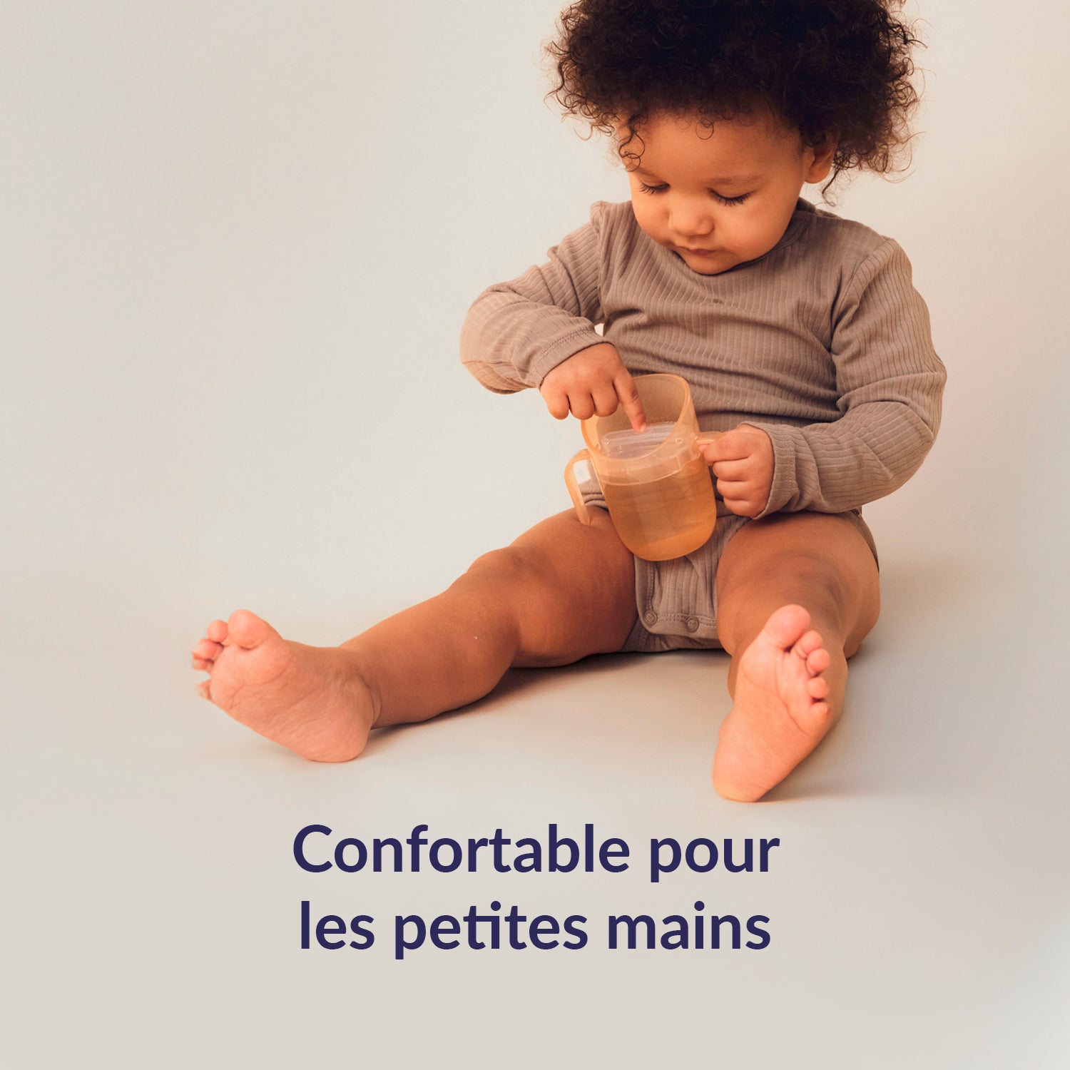 Petite fille est assise par terre et tient le gobelet d’apprentissage Difrax LOVI Genius – confortable et facile à saisir pour les petites mains