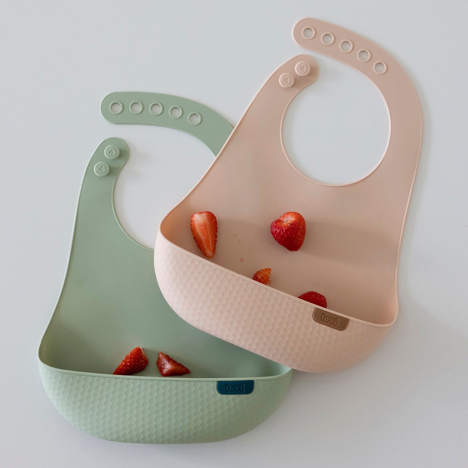 Bavoirs en silicone pour bébé, coloris nude et pistache, avec des fraises, présentés sur la page produit