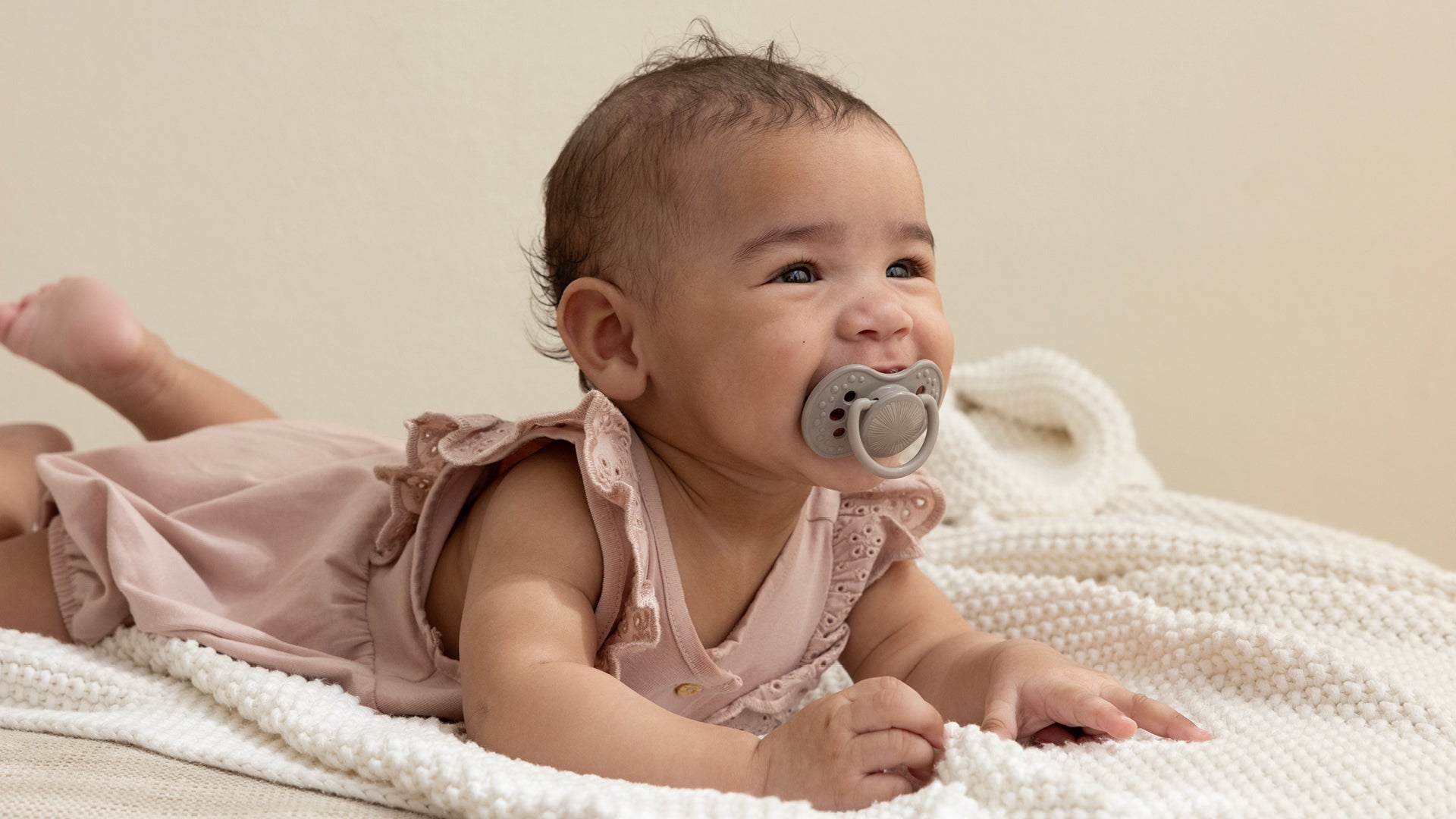 Bébé souriant allongé sur le ventre avec une tétine Harmony

