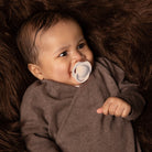 Un bébé heureux couché avec la sucette ivory dynamic dans la bouche