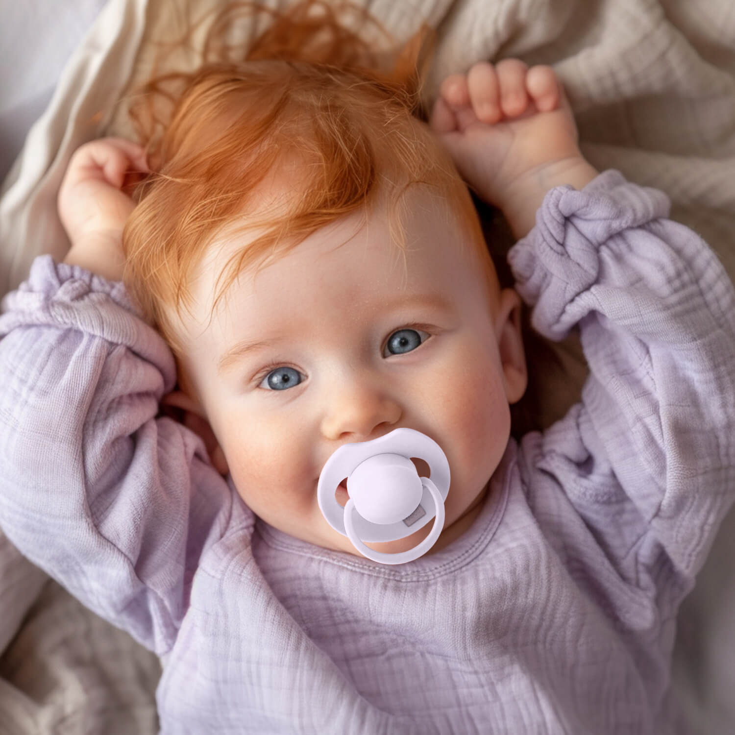 Un bébé heureux couché avec la sucette lila dynamic dans la bouche