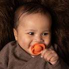 Un bébé heureux couché avec la  sucette Orange dynamic dans la bouche