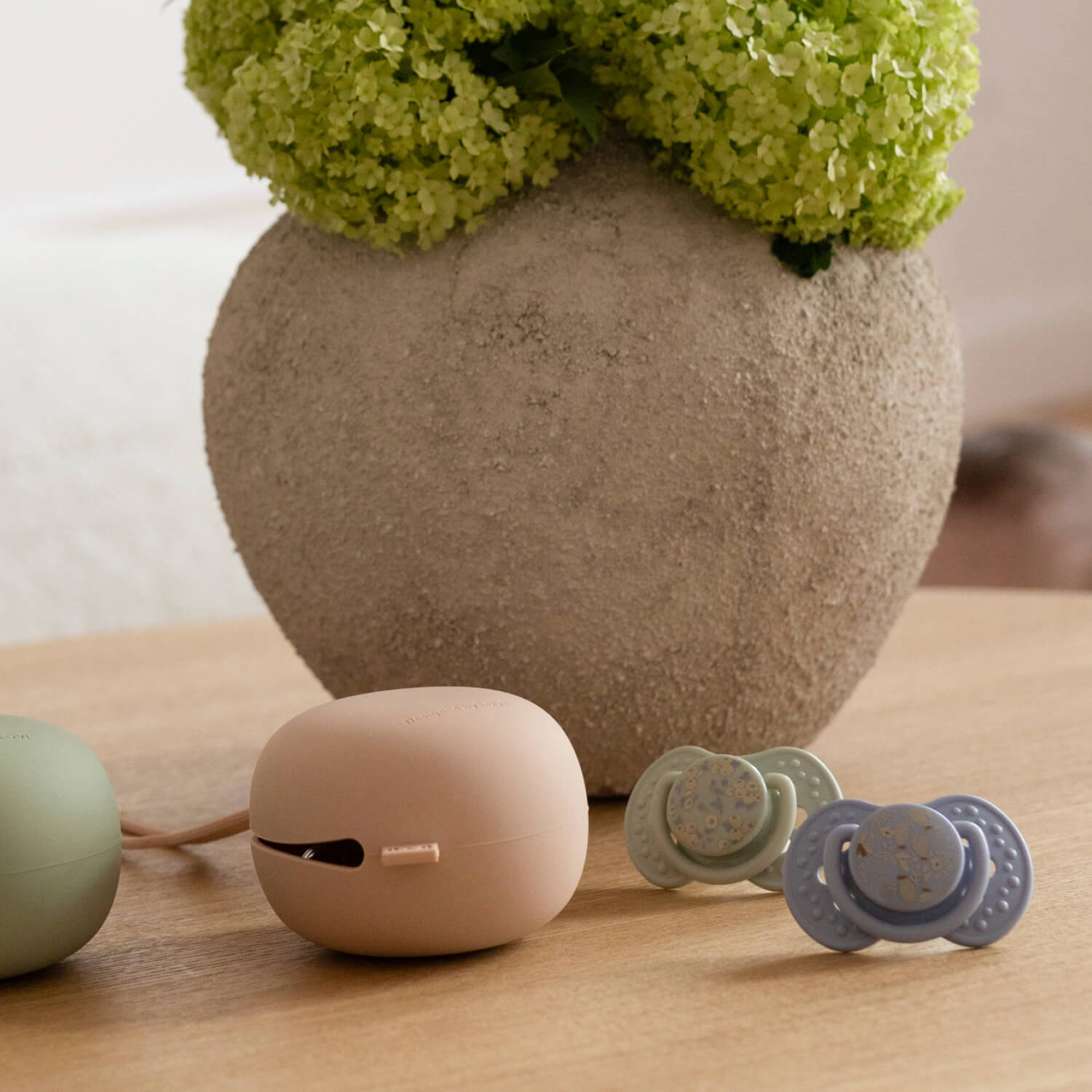 Photo d'ambiance des sucettes Difrax LOVI Blossom 18+ mois, Boy, 2 pièces, silicone, petit bouclier, anneau phosphorescent, sans BPA, avec des porte-sucettes en silicone en arrière-plan
