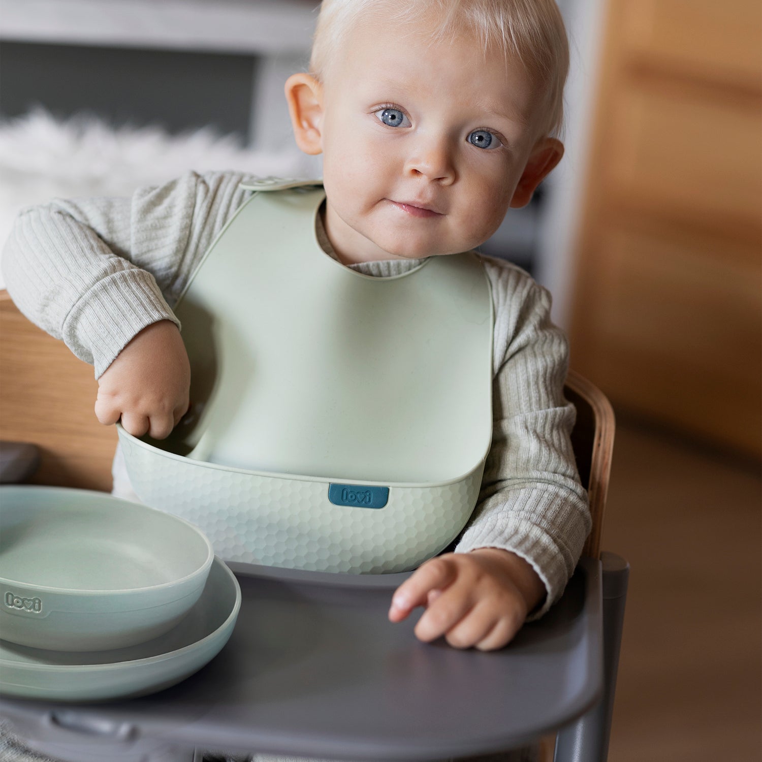 Enfant dans une chaise haute avec le bavoir en silicone et l’assiette devant lui – Difrax LOVI Baby Eet- & Drinkset Pistachio, repas hygiéniques et confortables.