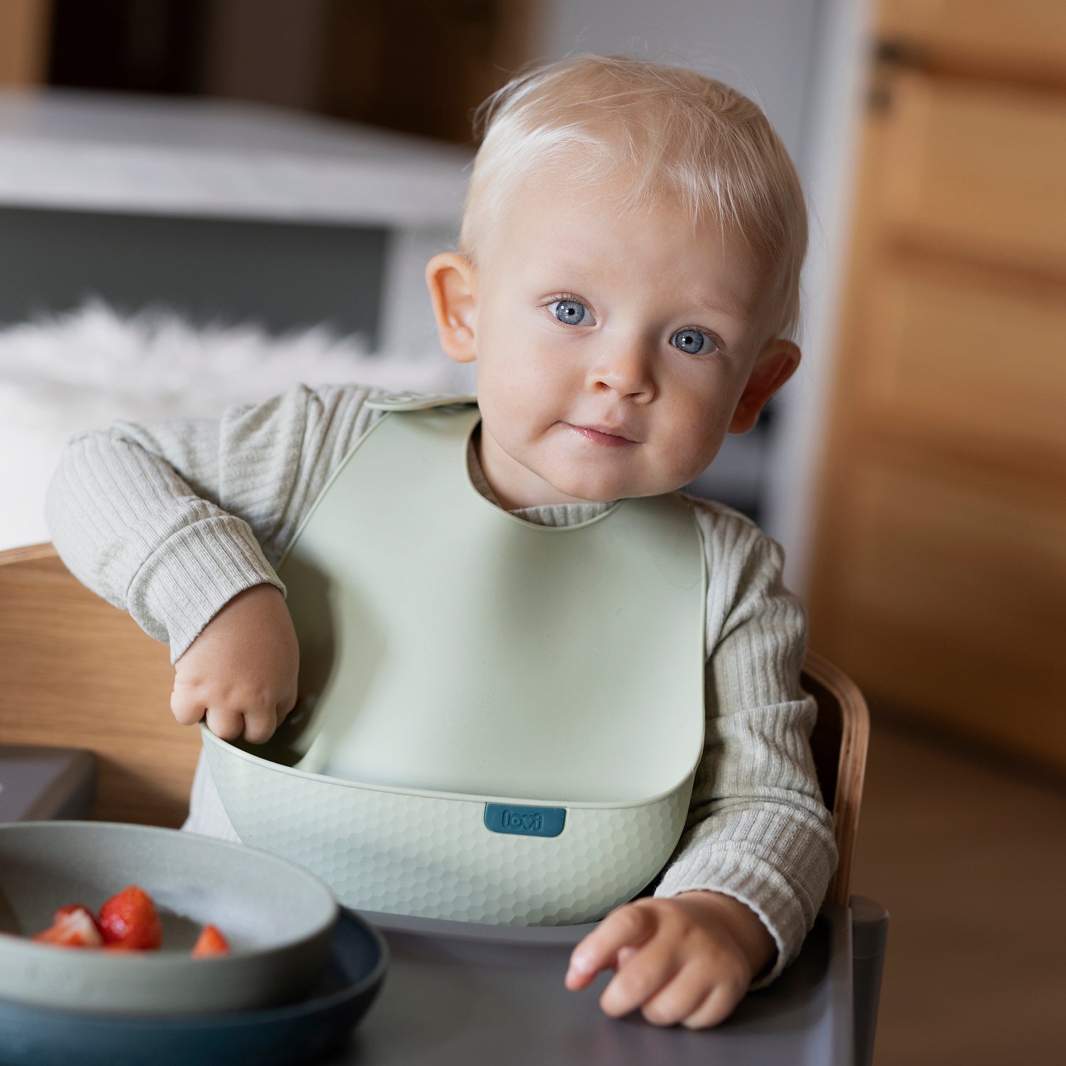Un enfant heureux est assis dans la chaise de bébé et savoure son repas avec la plaque en silicone de couleur pistache.