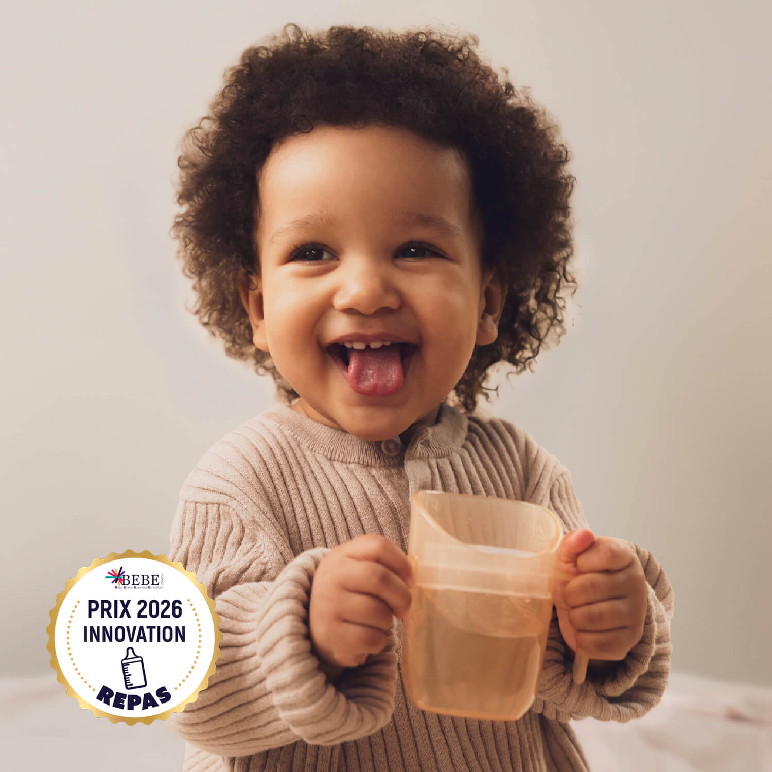 eune fille tient le Gobelet Genius Difrax LOVI en couleur Nude, lauréat du Prix Innovation 2026, adapté pour apprendre à boire de manière autonome dès 6 mois.