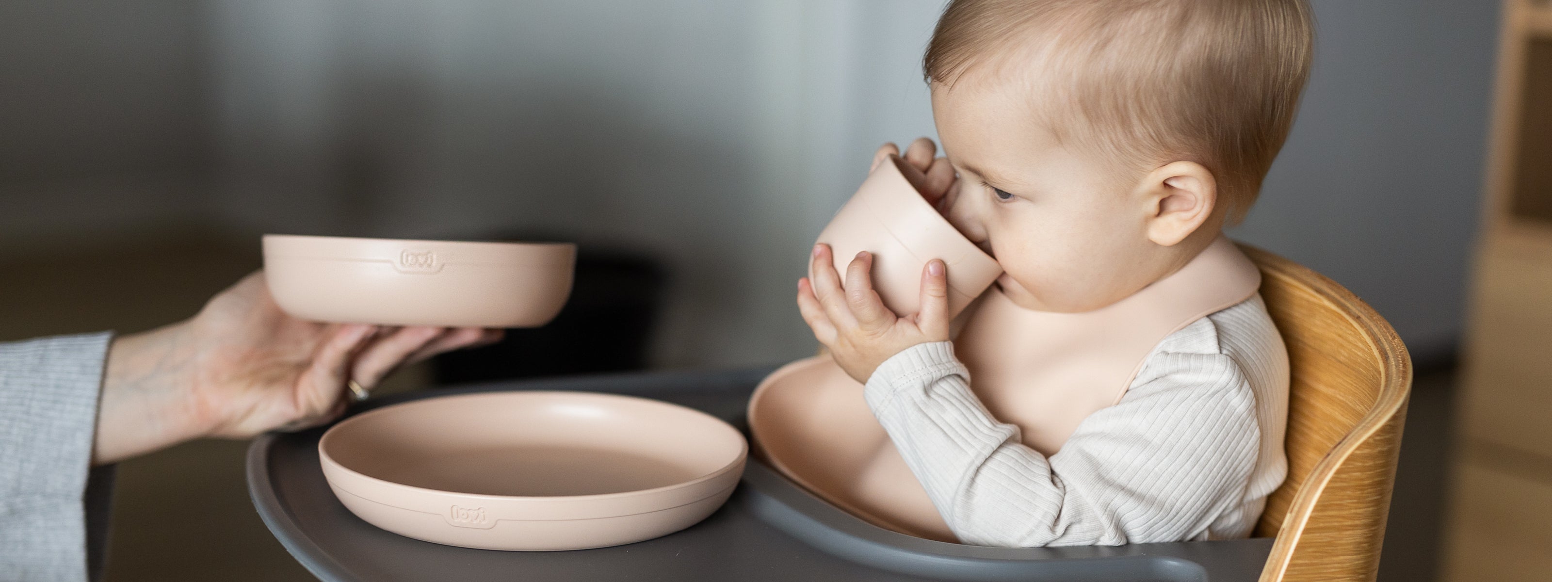 Enfant assis dans une chaise haute buvant dans la tasse du set repas bébé, léger et maniable