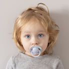 Un petit garçon heureux assis avec la Sucette dynamique Prime babybleue