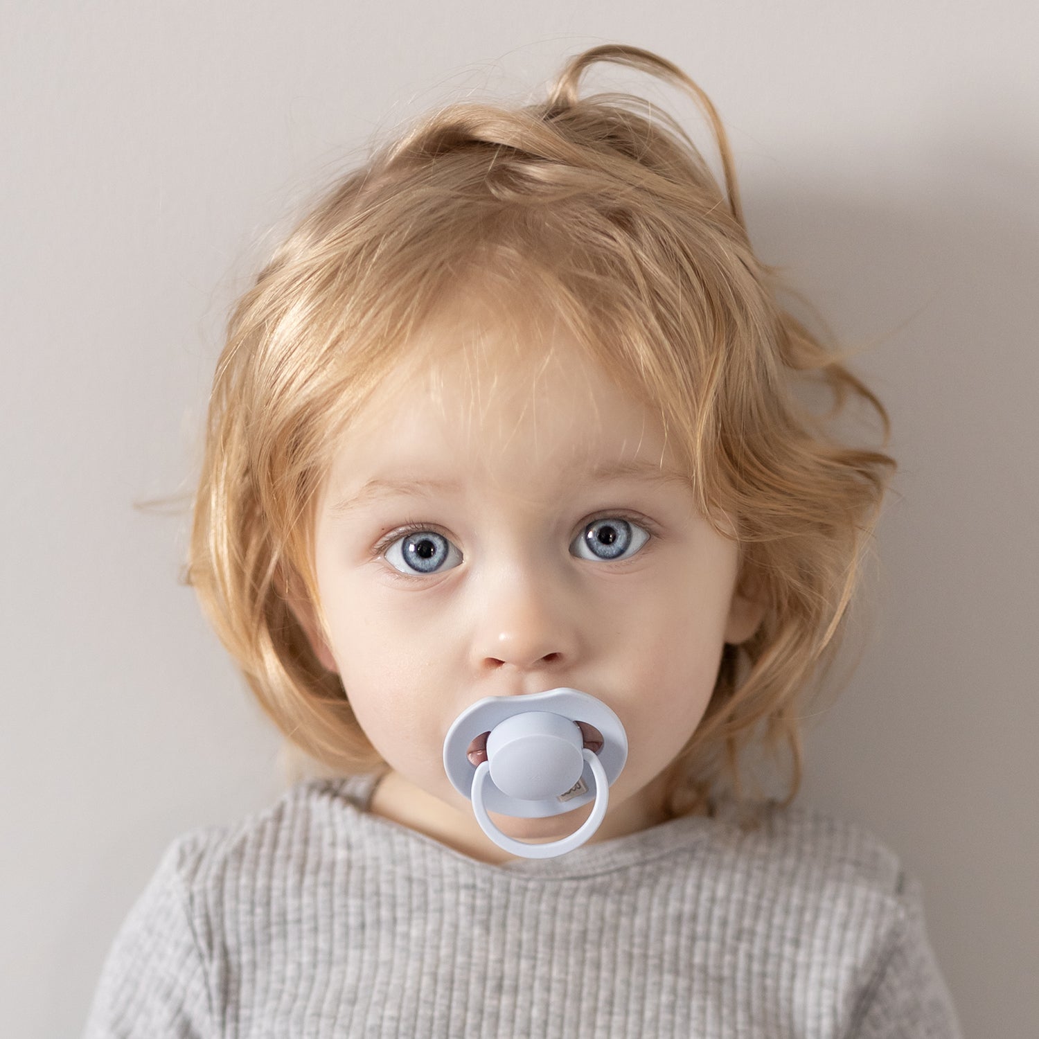 Un petit garçon heureux assis avec la Sucette dynamique Prime babybleue