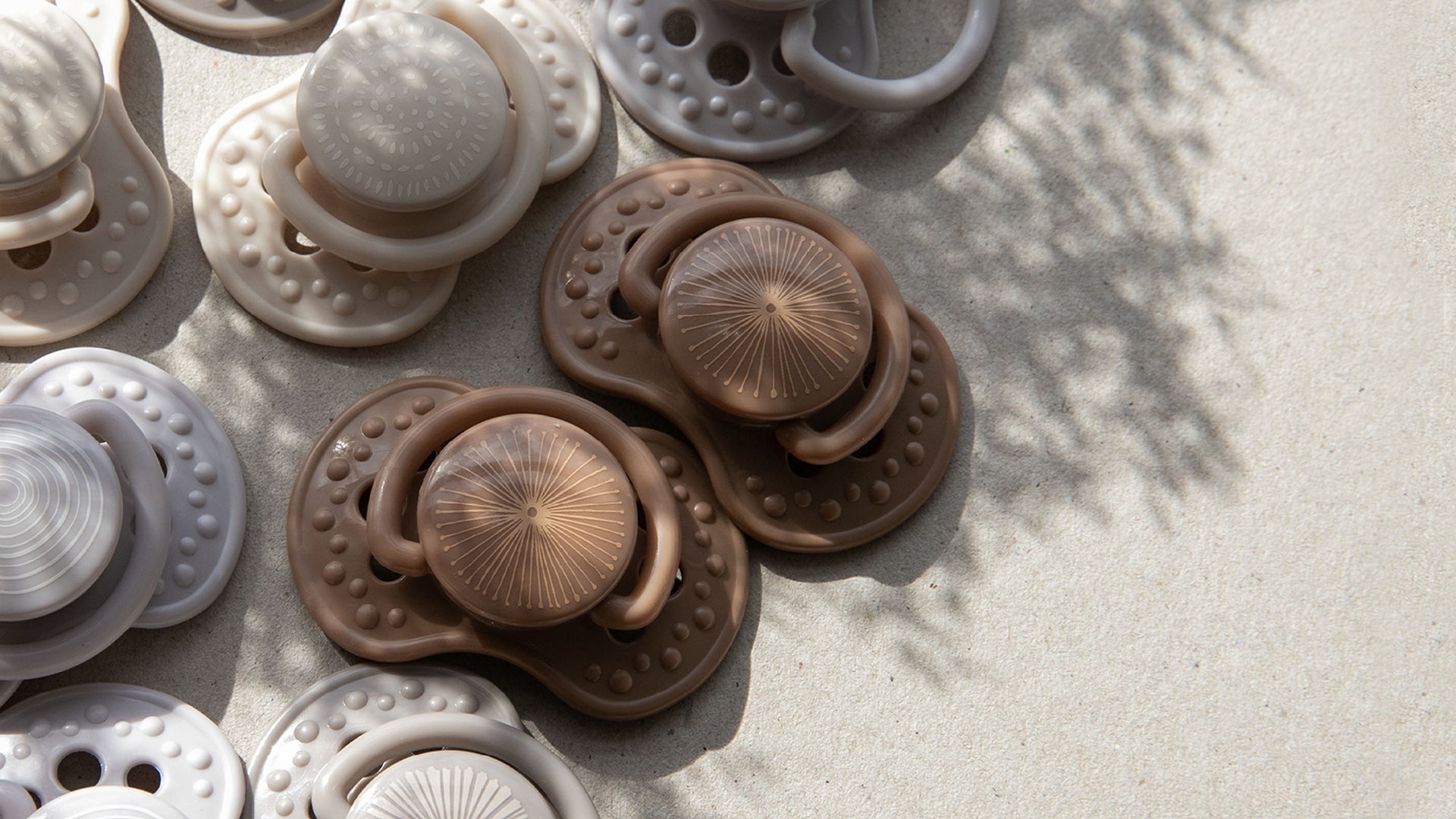 Tétines de la collection Harmony en brun, beige et gris, présentées sur la page contact